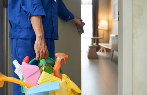 unrecognizable-cleaner-walking-into-hotel-room-with-tools-detergents